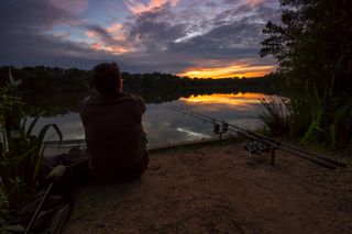 Angler watching the sunset sat next to some fishing rods