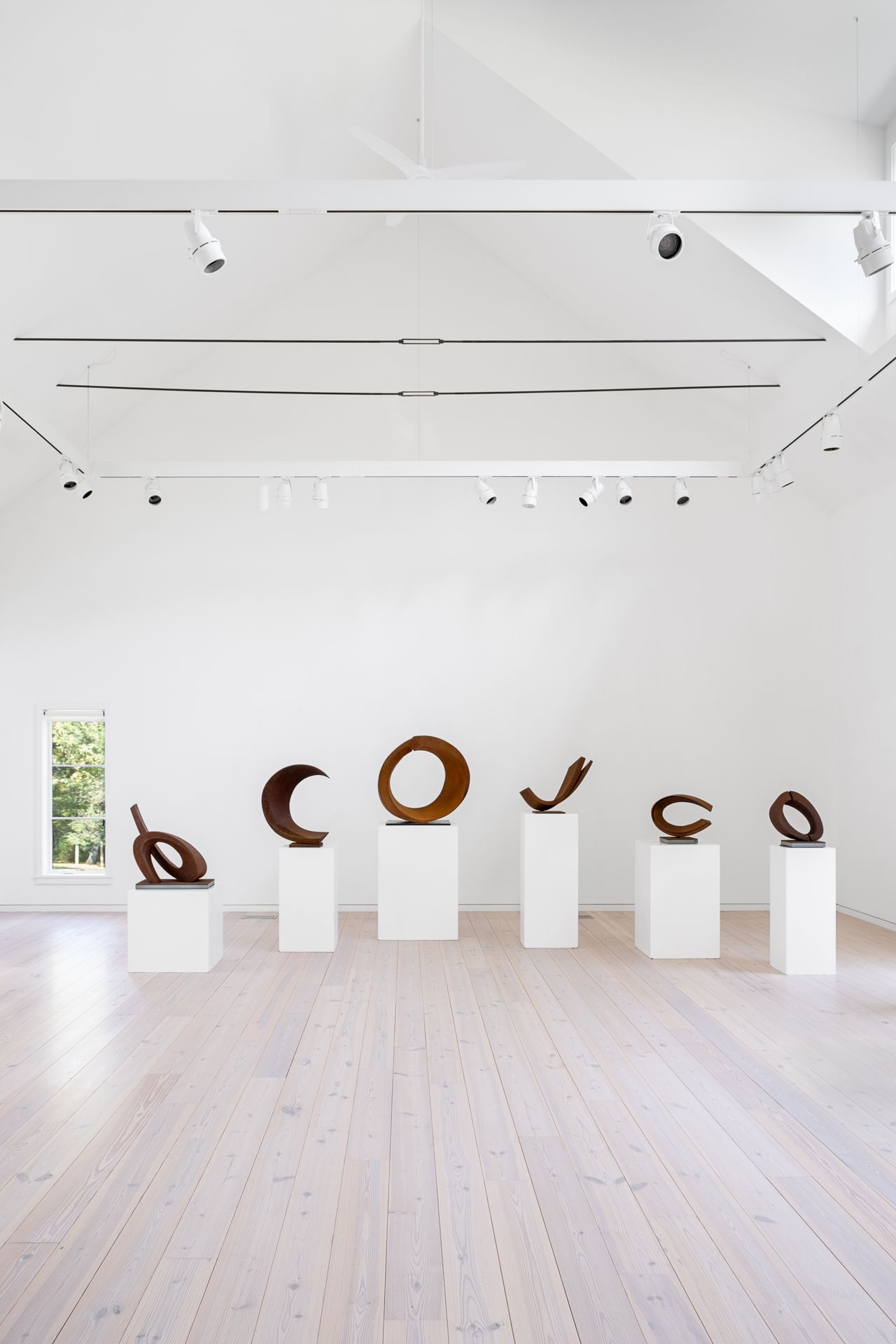 Installation view of a sculptural solo show in a gallery, featuring arched structures carved from copper displayed on white, iron, and beige pedestals in an otherwise white-cube kind of space.