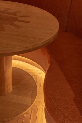 A detail photograph of a wooden table and a fabric sofa renders the warm, orangey atmosphere of a modernly furnished restaurant.