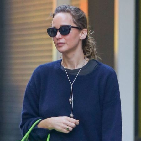 Jennifer Lawrence steps outside wearing a navy jumper with blue jeans, brown suede mules and an apple green leather bag.