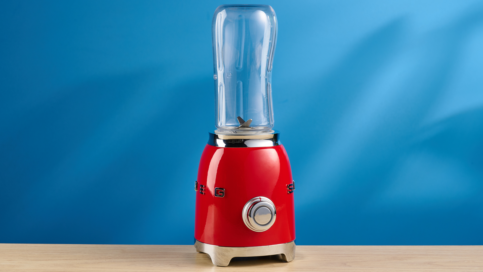 Smeg Personal Blender in the red colorways photographed in front of a blue background.