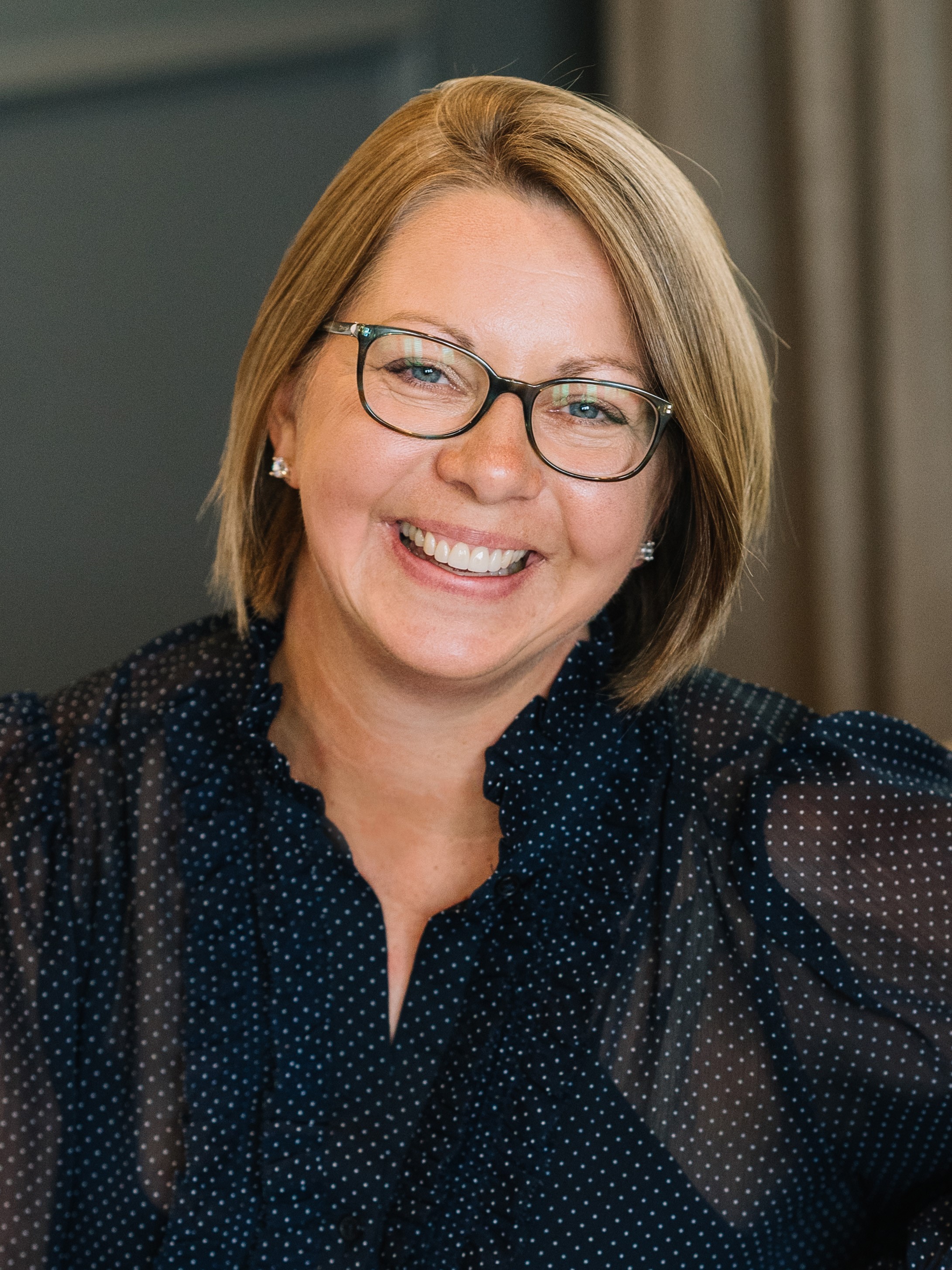 A headshot of a woman with a blonde bob and glasses