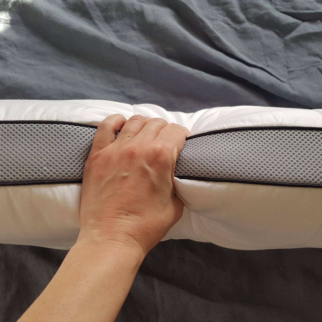 The Panda Hybrid Bamboo pillow on its side with the grey mesh edge squeezed by a hand