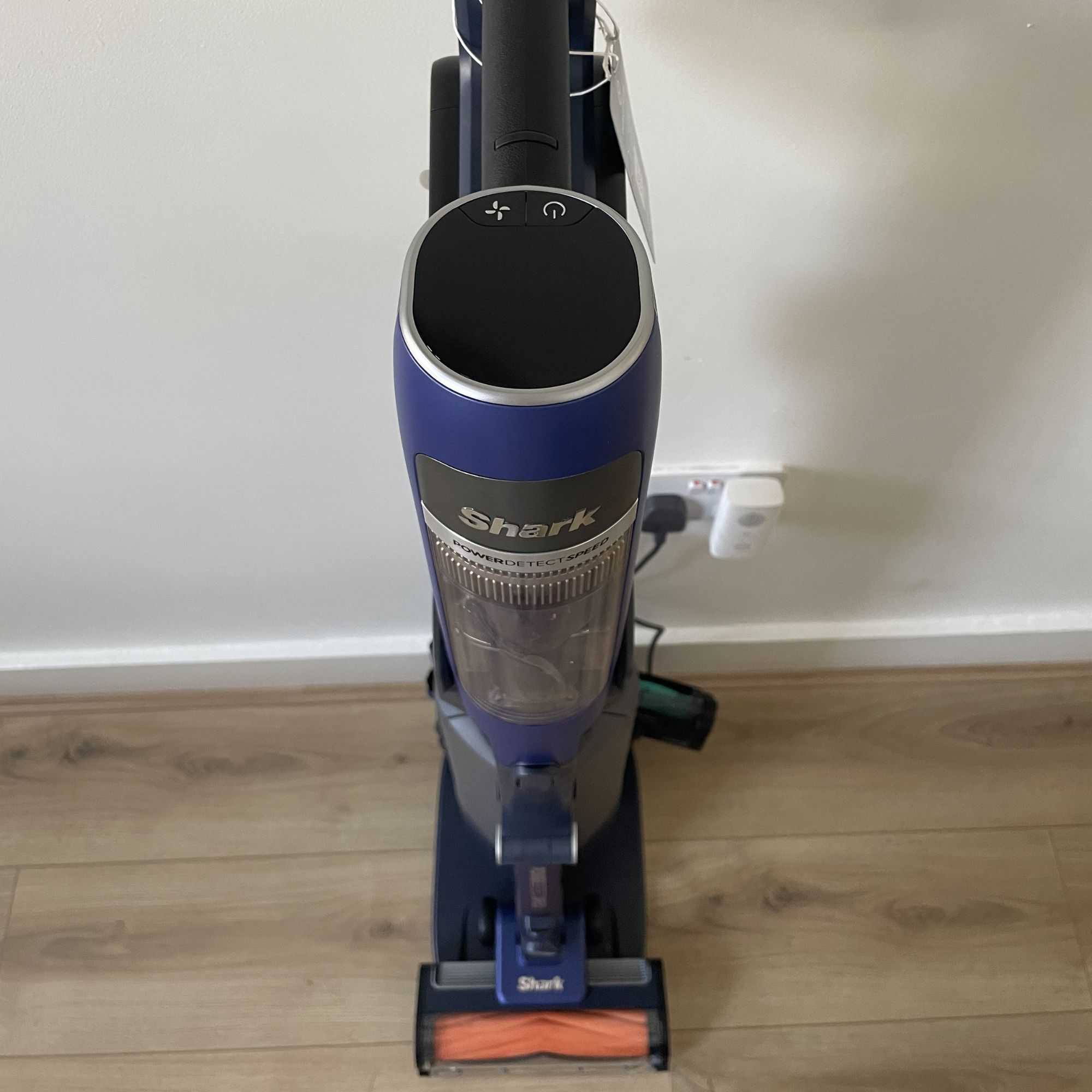 The Shark PowerDetect Speed Clean and Empty from above, seen as it stands in front of a white wall on wood-effect flooring