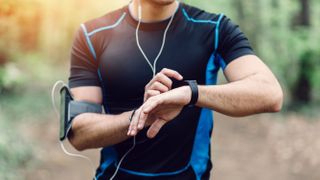 Man checking GPS sports watch while running in woodland