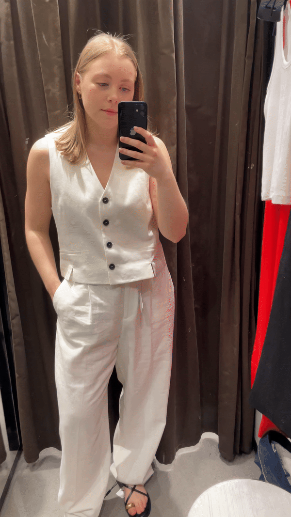 Woman in dressing room wears cream waistcoat, cream trousers