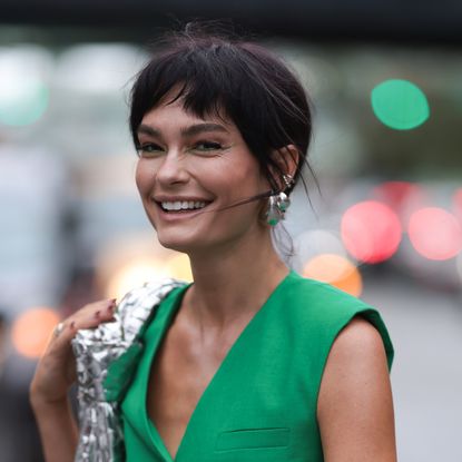 Quigley Goode wearing green waistcoat, silver bag and earrings and the best eyeshadow stick look