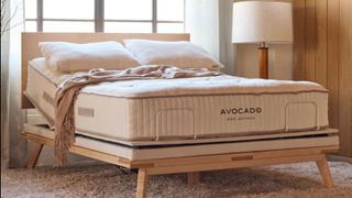 The image shows the Avocado wool mattress on a wooden bedframe in a neutrally decorated bedroom