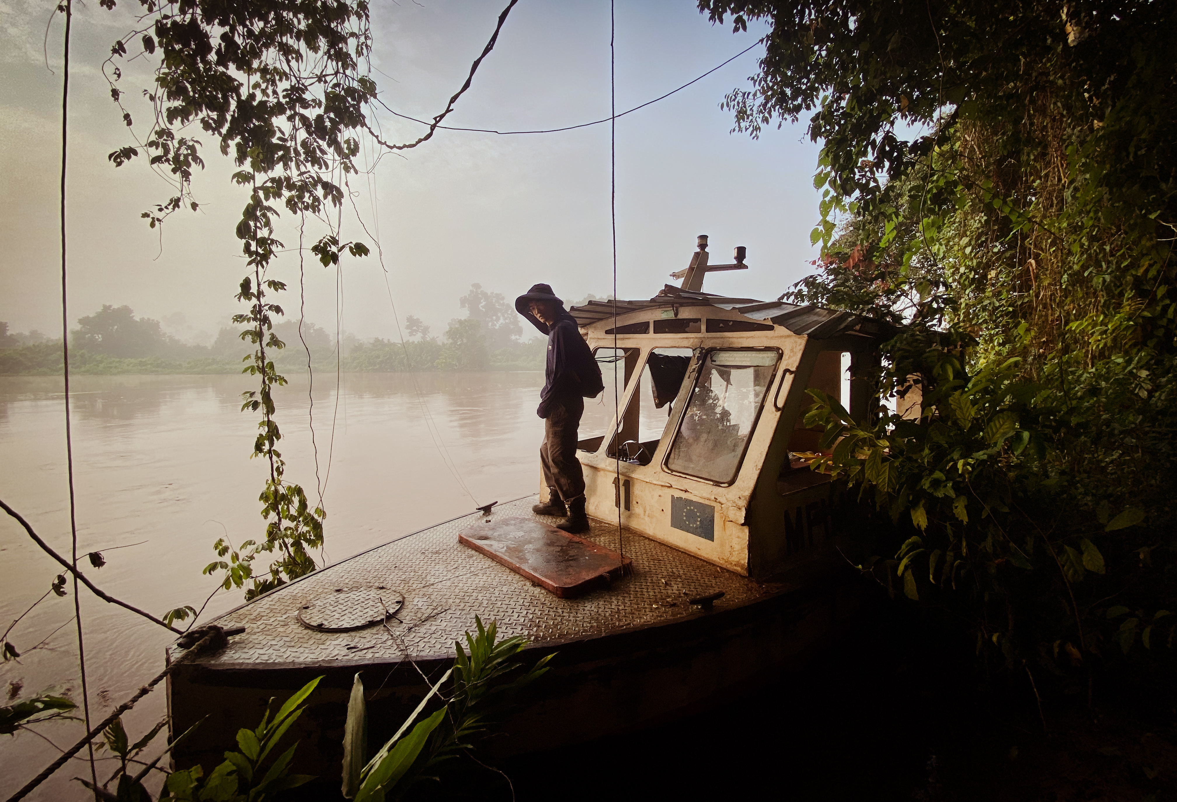 A scientist stands on the front of a small research boat on the shores of a blackwater lake in the Congo Basin.