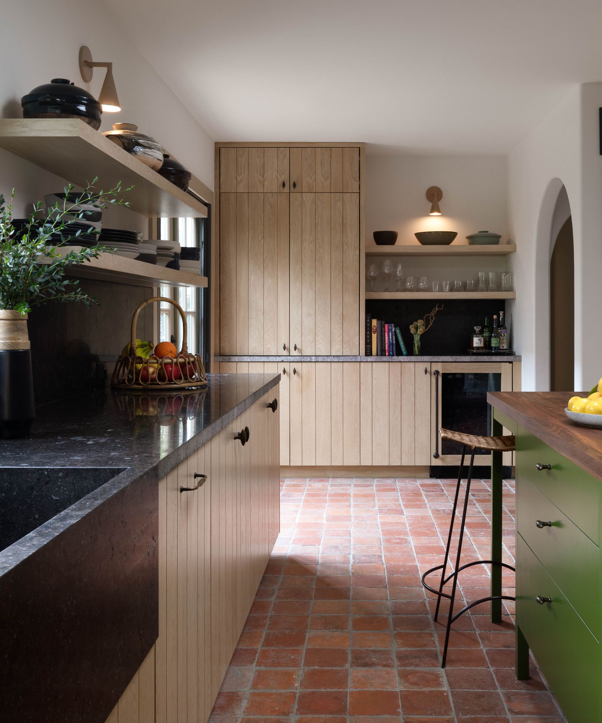 A country kitchen with wood cabinets, granite countertops, terracotta floor tiles, and a green island