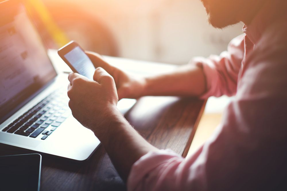 Man looking at smartphone while seated at laptop