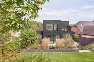 A modern home with burnt timbre cladding and landscaped gardens in the foreground