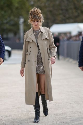 A woman wearing a party dress, trench coat and knee high boots