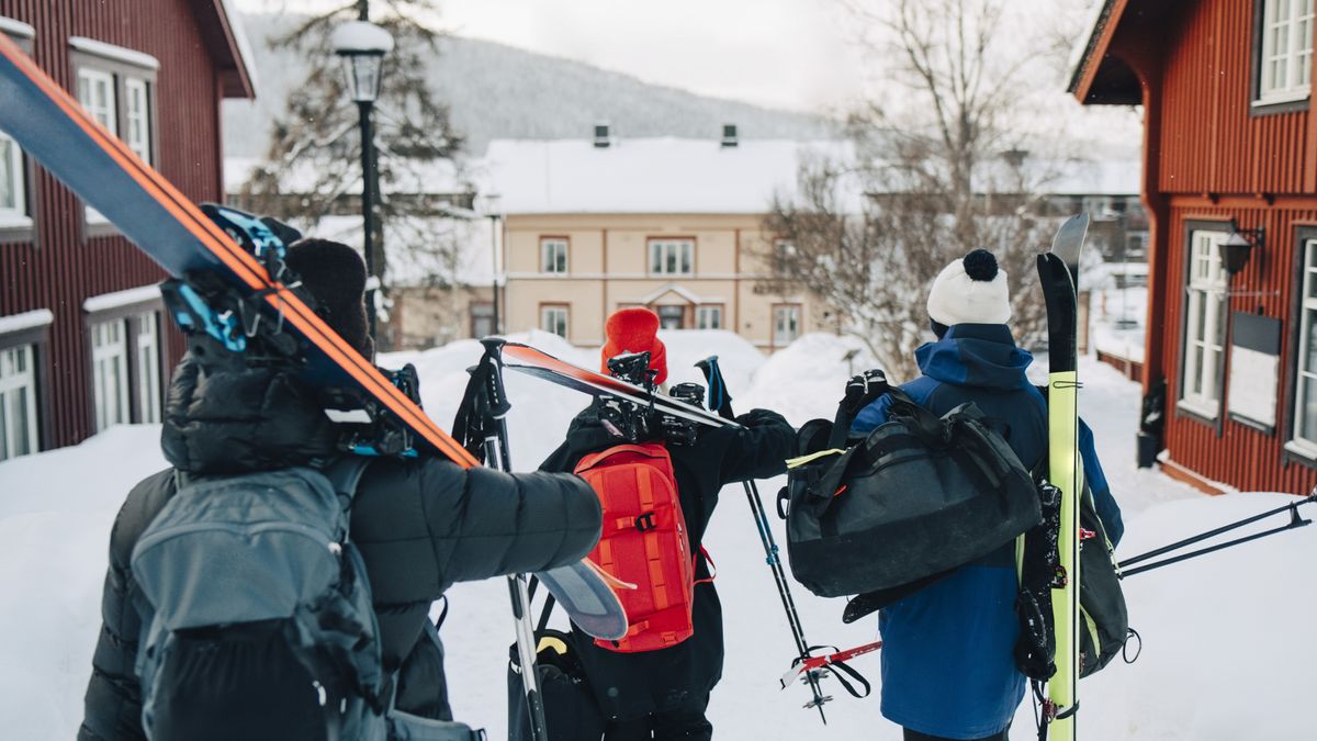 Three skiers walking through a resort with skis over their shoulders