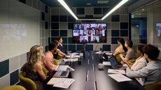 A photo of a business team gathered in a boardroom to run through a tabletop exercise and discuss cybersecurity strategy. At the far end of the boardroom table, more colleagues are seen on a video call.