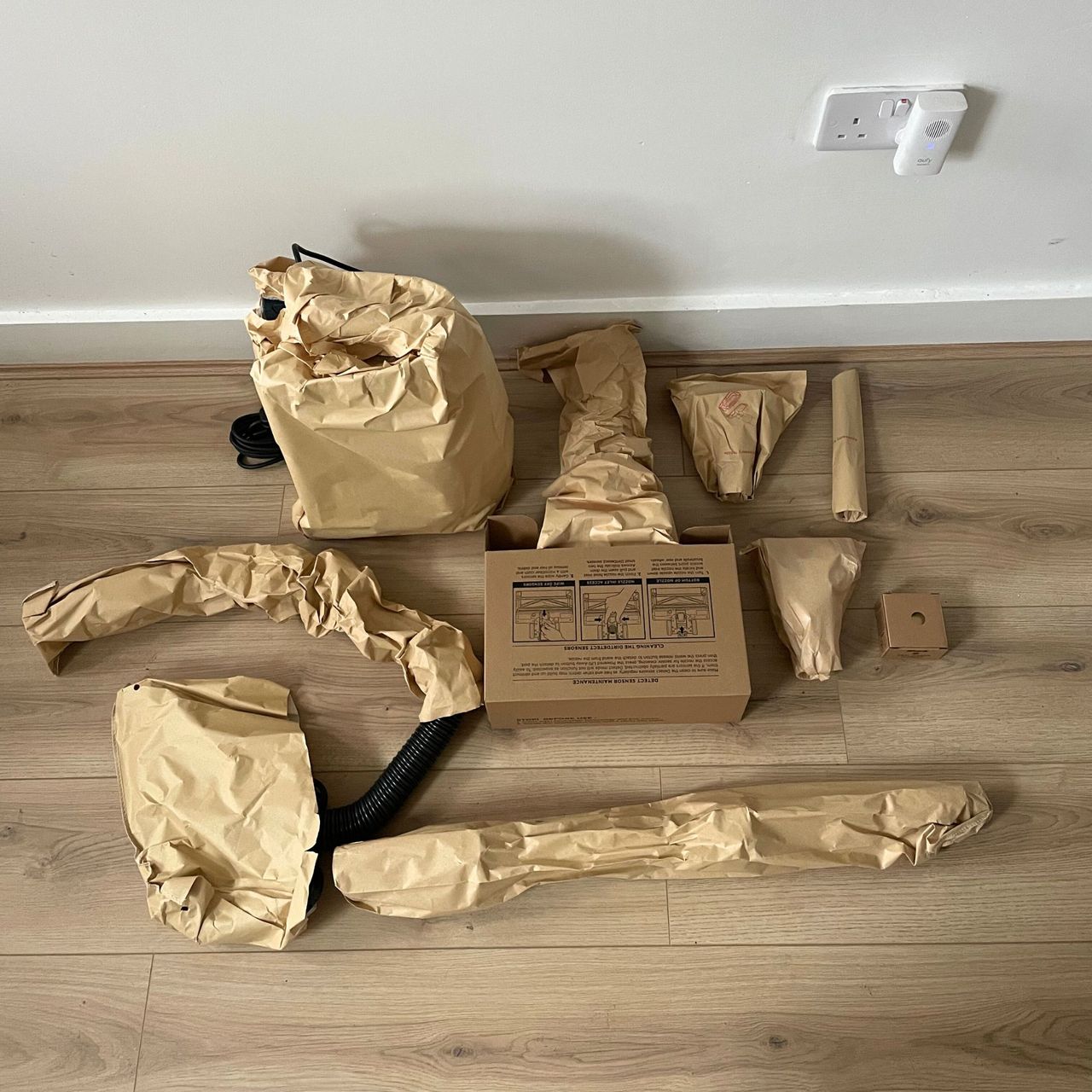 components of the Shark PowerDetect Powered Lift-Away Upright Pet Vacuum Cleaner AZ3900UKT wrapped in paper and laying on wood-effect flooring