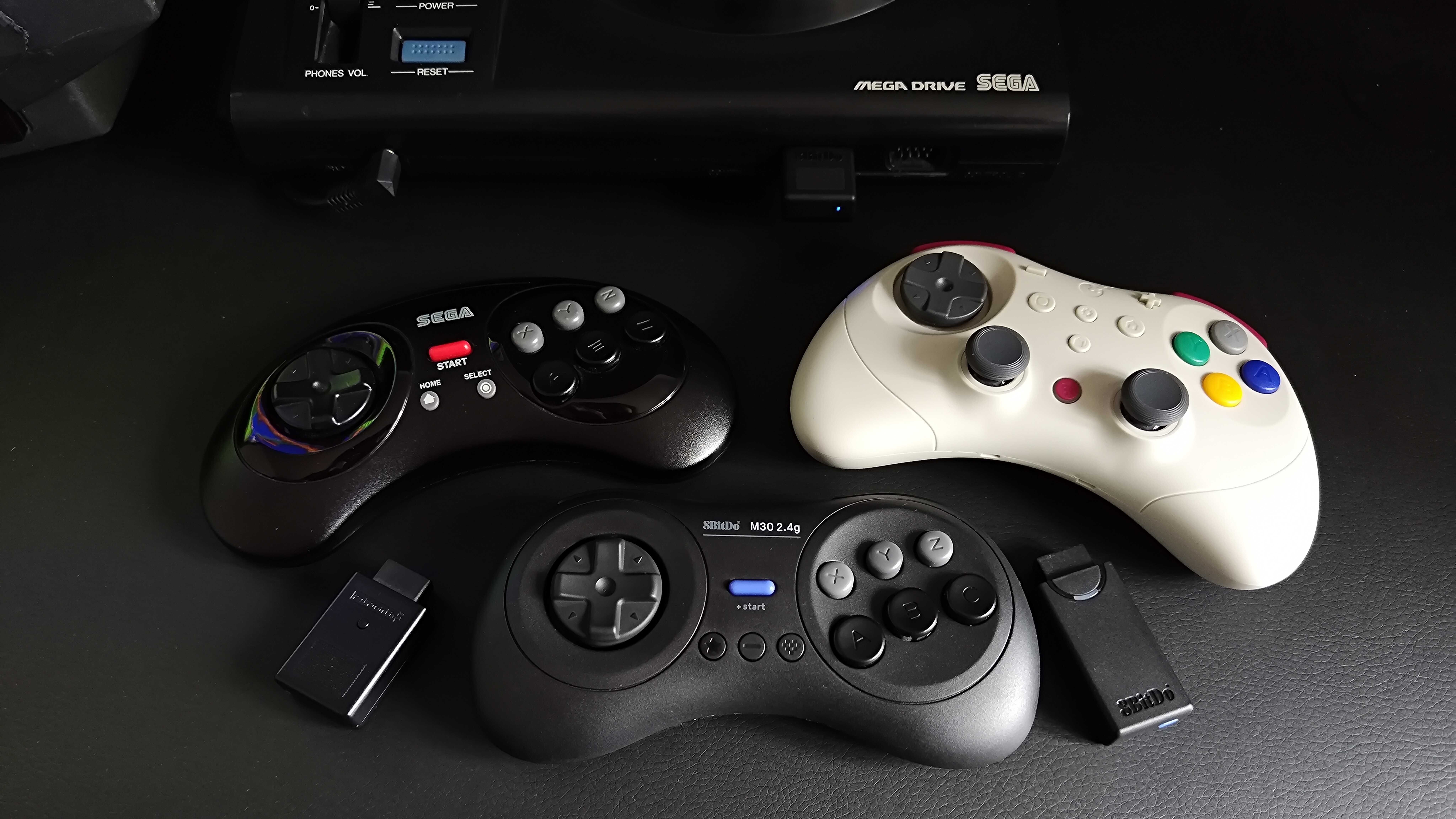 Retro-Bit Sega Mega Drive controller on left, Gullikit Elves 2 Pro on right, and 8Bitdo M30 in middle next to receivers in front of Japanese console.