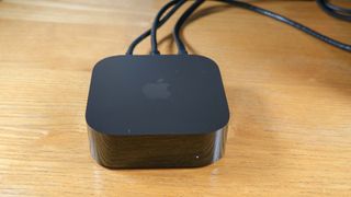 The Apple TV 4K (2022) is on a wooden surface, with cords coming out of the back.