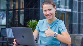 smiling person freelancer outdoors working on laptop computer MacBook by Apple with smartwatch Apple Watch, iPhone smiling, show thumb up, like gesture.