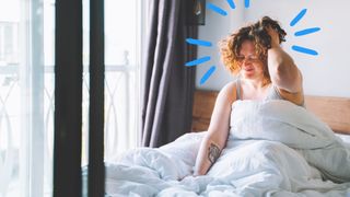 A woman waking up to exploding head syndrome, holding her head in frustration