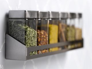 A spice rack hanging on a wall with various spices in glass jars.
