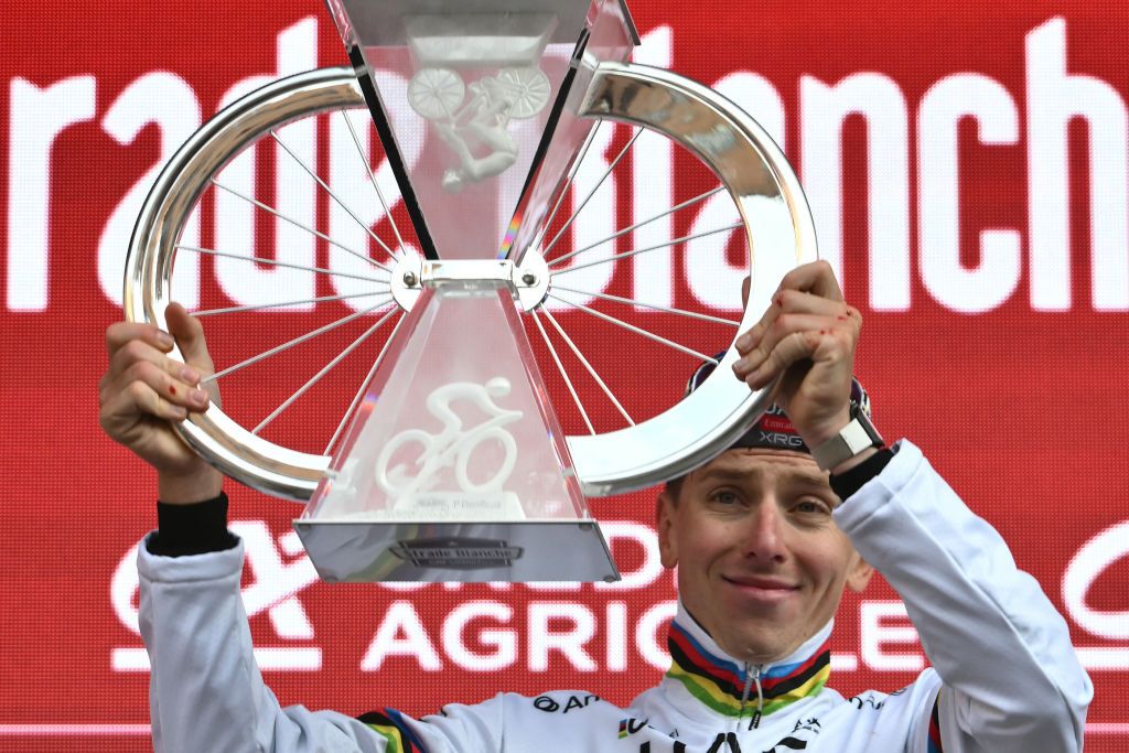 Team UAE's Slovenain rider Tadej Pogacar celebrates as he holds his trophy on the podium after winning the 19th one-day classic 'Strade Bianche' (White Roads) men's cycling race between Siena and Siena in Tuscany on March 8, 2025. (Photo by Marco BERTORELLO / AFP)