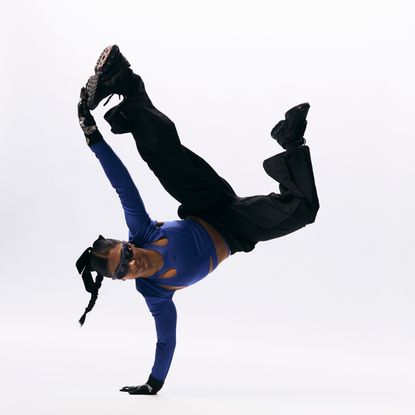 a breakdancer performs a skill while wearing baggy pants and a crop top