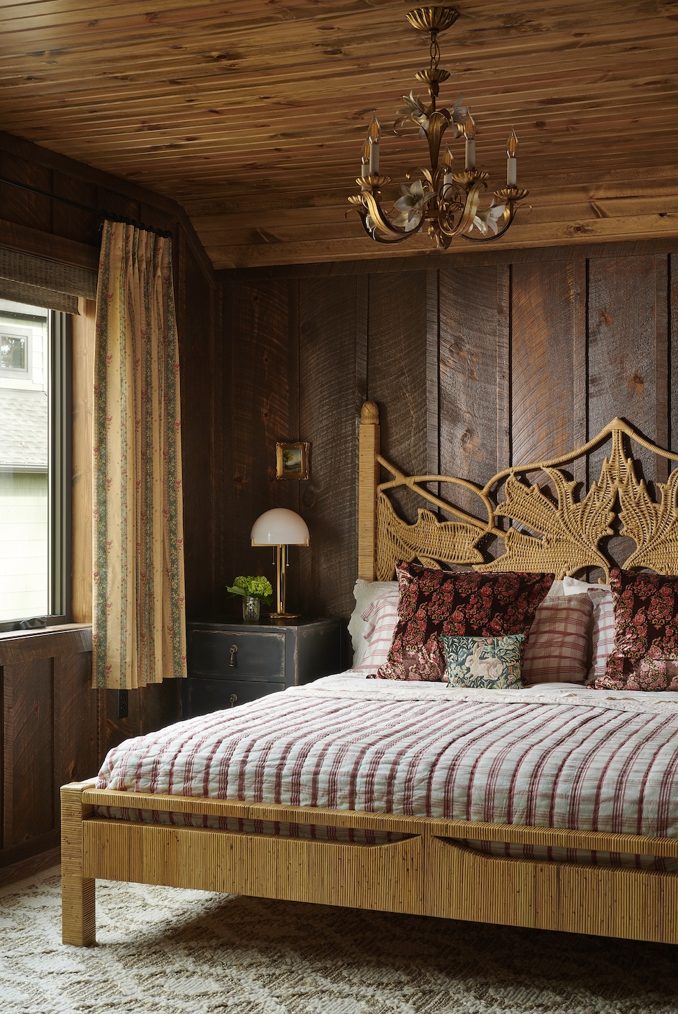 A bedroom with a rattan bed frame, dark wood-paneled walls and ceilings, and short curtains.