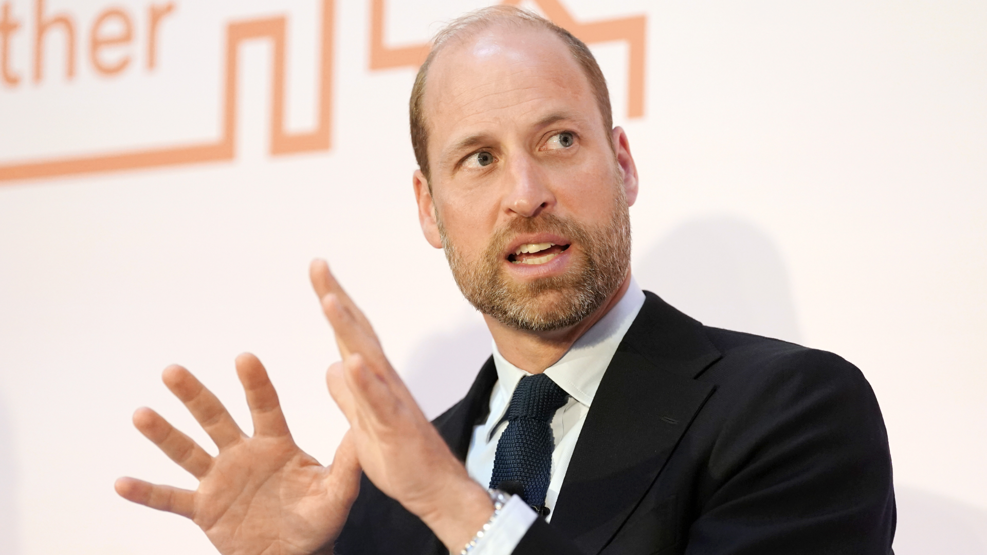 Prince William wearing a black suit and talking while gesturing with both hands