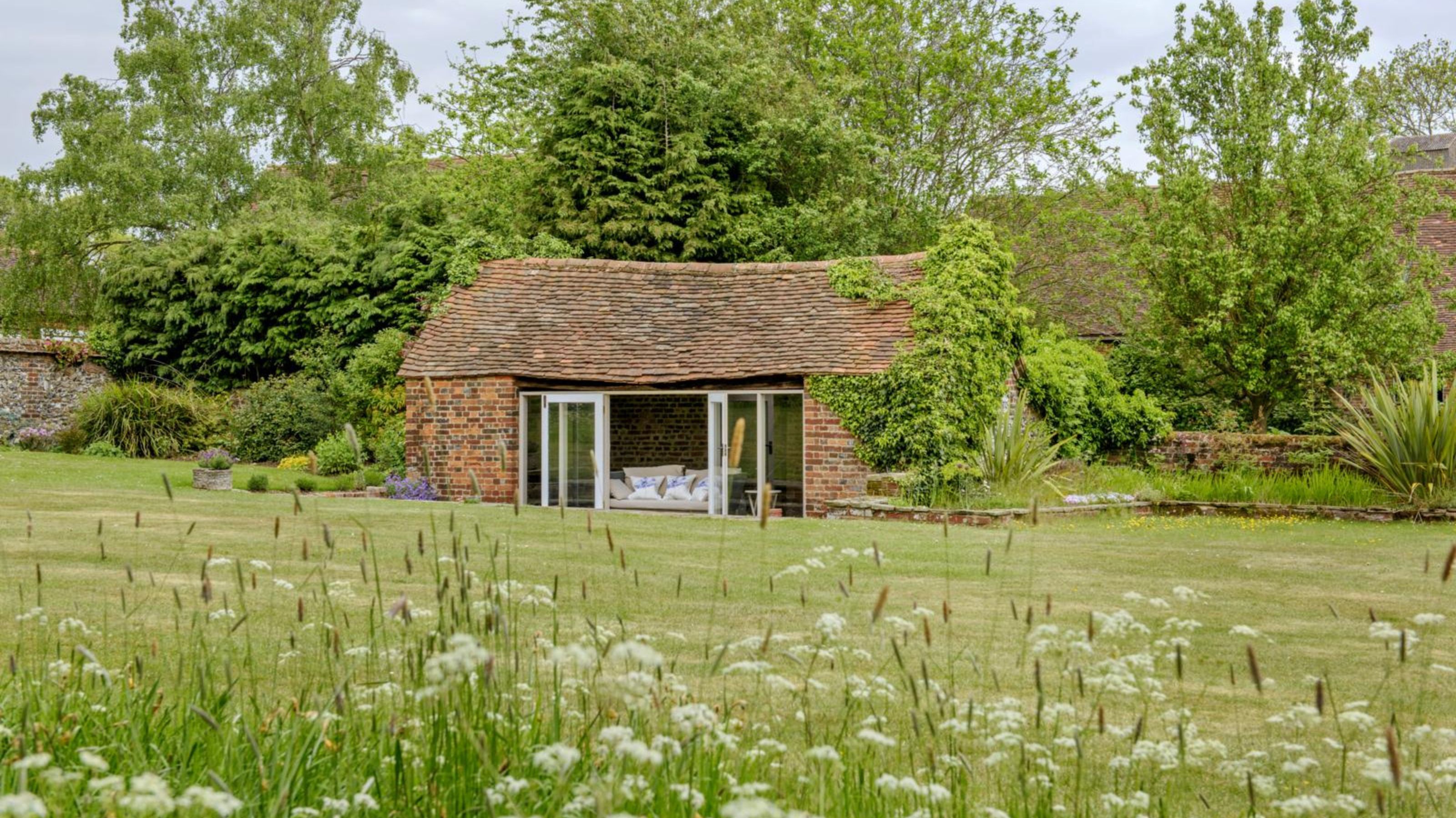 A cottage surrounded by long grass and meadow flowers