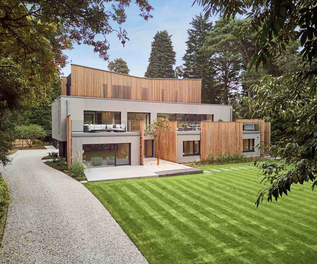 A contemporary self build set over three storeys surrounded by woodland and an extensive lawn. The house is clad in grey render and timber and features an interesting butterfly-style roof.