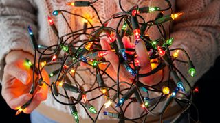 A person holds a knotted ball of Christmas lights. 