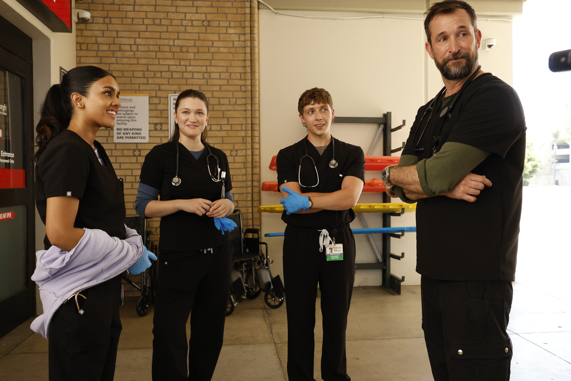 Shabana Azeez, Isa Briones, Gerran Howell, Noah Wyle as doctors standing around the entrance of a hospital in the pitt season 2