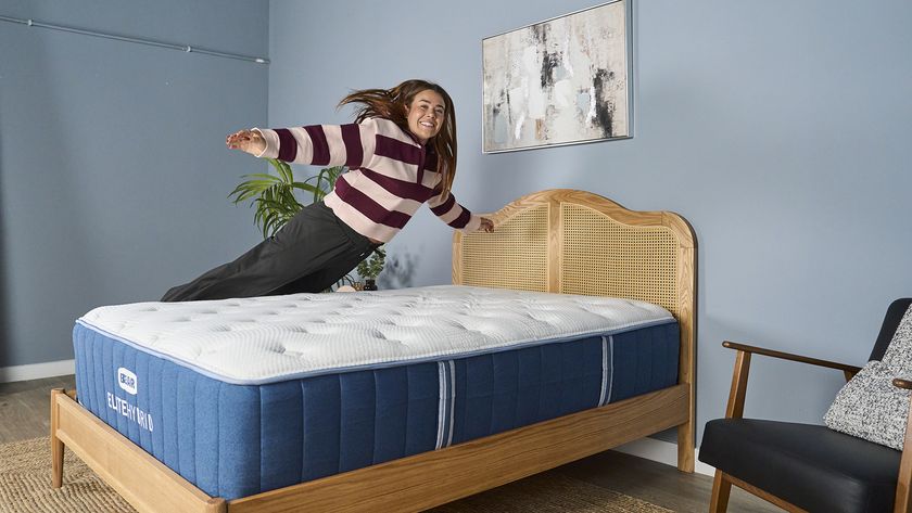 Our mattress tester jumping on the Bear Elite Hybrid mattress on a wooden bedframe with a rattan headboard in our sleep studio with blue walls and a bedside plant