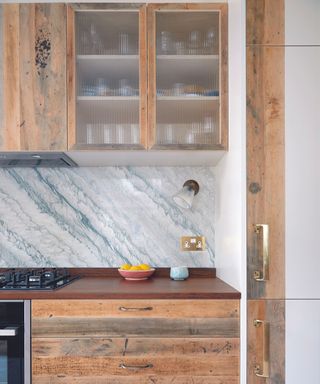A kitchen with marble backsplash and natural wooden cabinetry