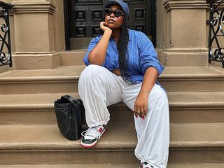 influencer aniyah morinia sits on stairs of a stoop while wearing blue and white striped button up and white pants with sneakers