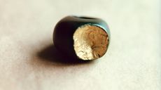 A close-up of a green circular button with a front-side chunk removed showing the wood material. 