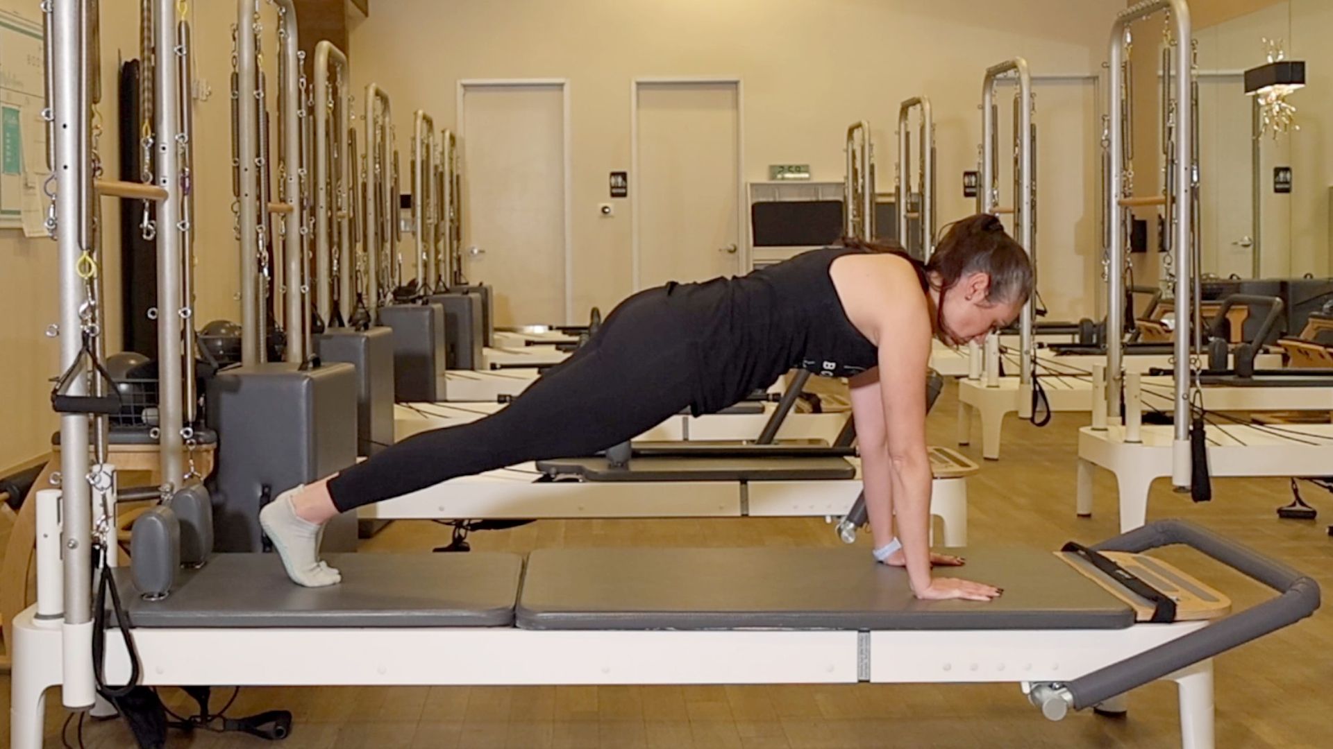 Woman demonstrating a Pilates exercise on the carriage of a Pilates reformer machine