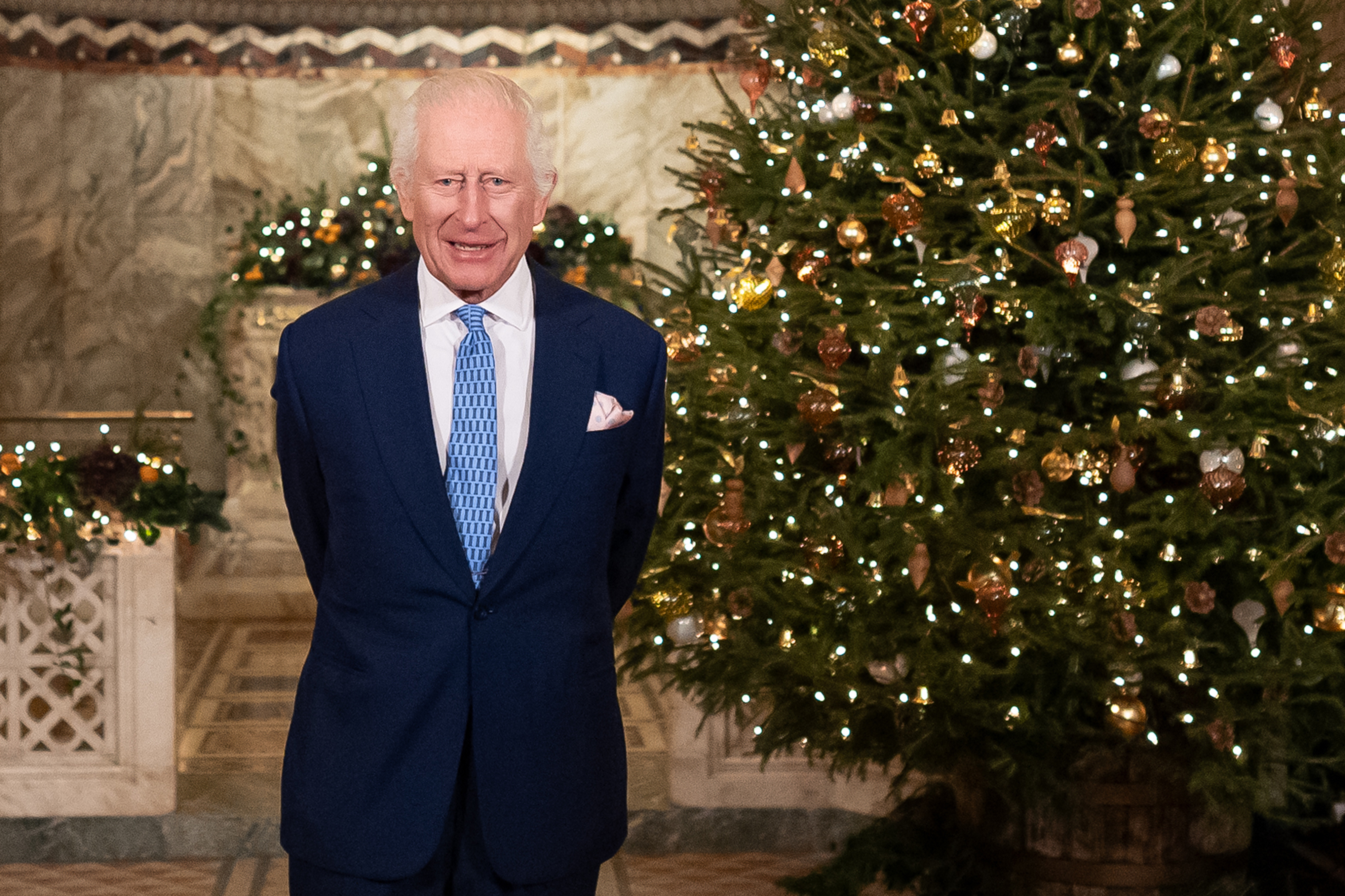 King Charles standing next to a Christmas tree