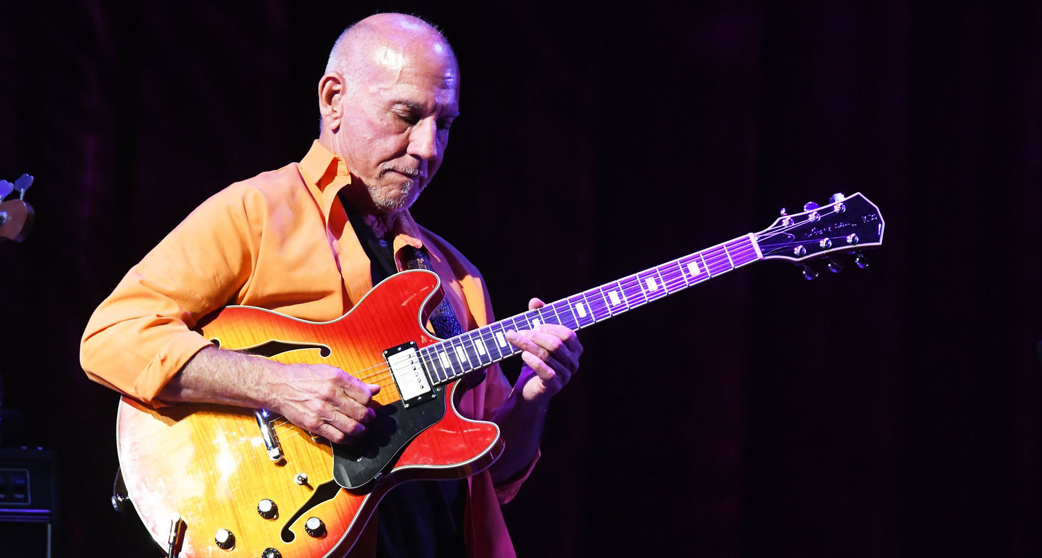 Larry Carlton wears an orange shirt and takes a solo on a cherry burst semi-hollow live in Japan.