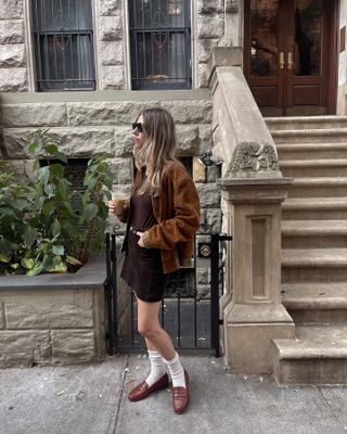 Robin Reetz wearing a chic fall outfit in New York City, including a brown suede jacket, miniskirt, loafers, and socks.