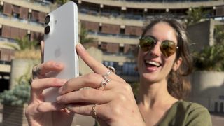 Person holding up an Apple iPhone 16 in both hands to take a photo and smiling widely