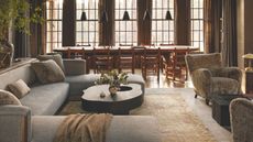 Moody farmhouse living room-dining room combo, featuring neutral, texture-rich furniture, large windowpane panels and a row of rustic pendant lights
