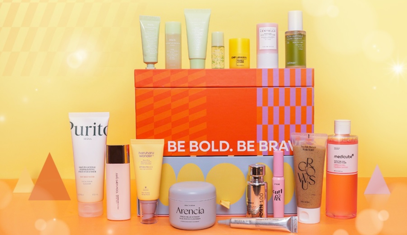 Yellow and orange background with an orange box and scattered images of beauty products on top of and in front of it