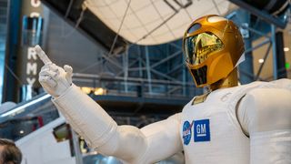 closeup photo of a white humanoid robot with a gold helmet in a museum exhibit hall