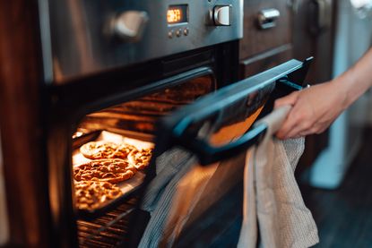 Hand opening the oven door while baking cookies in the oven