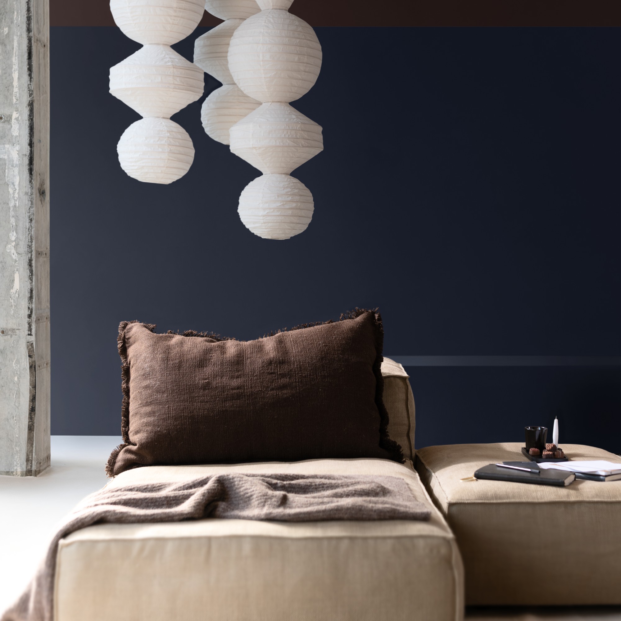 A living room painted in Dulux&#039;s Slow Swing dark blue shade with a modern modular sofa and paper lantern-style pendant lampshades