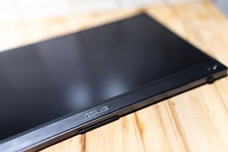 A black ASUS ZenScreen GO MB16AWP portable monitor sitting on a light wooden desk