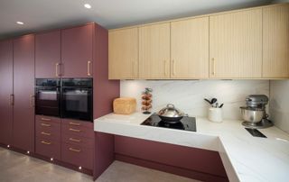 burgundy and wood kitchen cabinets with light coloured corian worktop 