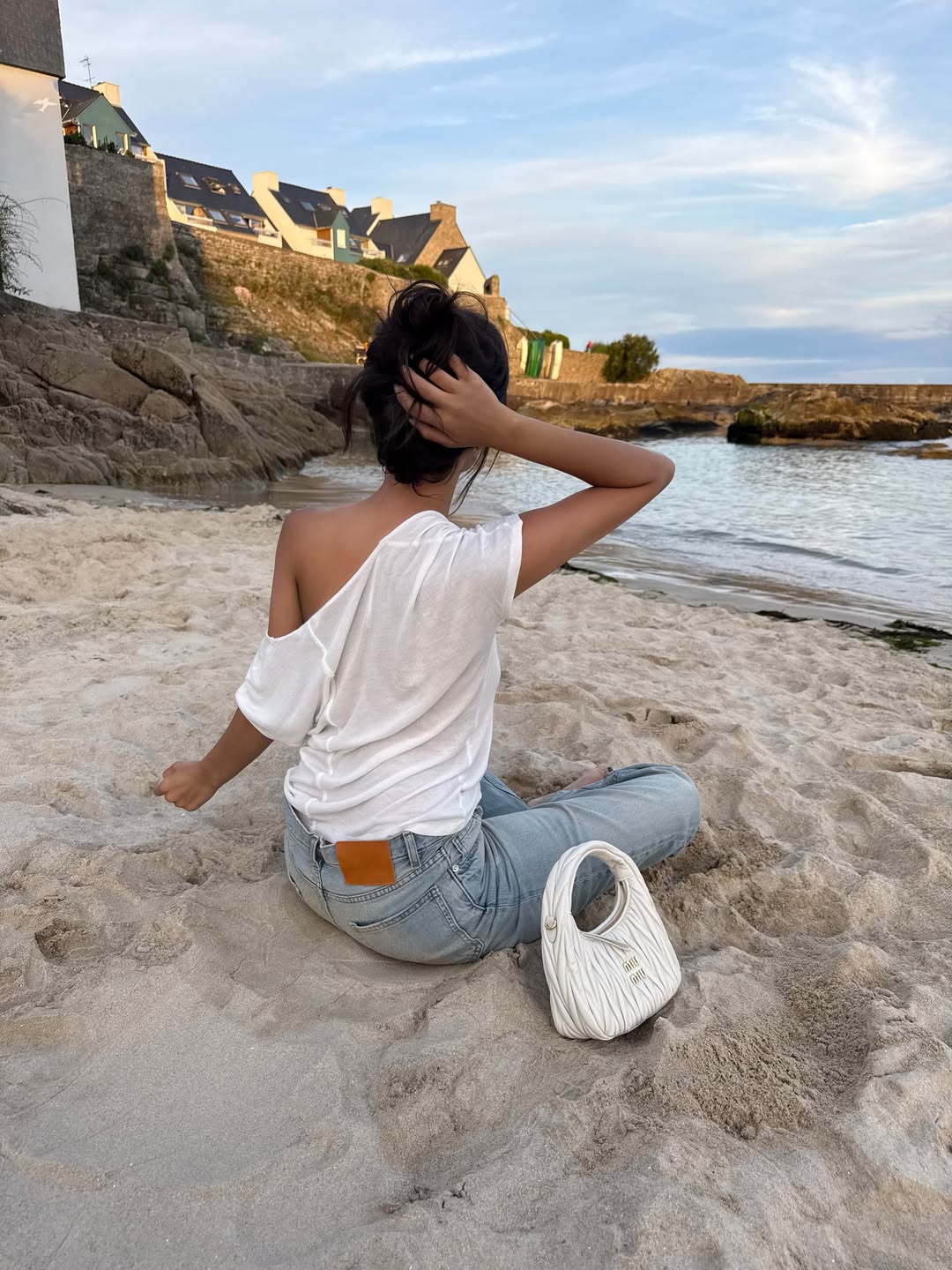 Elie in light-wash jeans and a white off-the-shoulder top